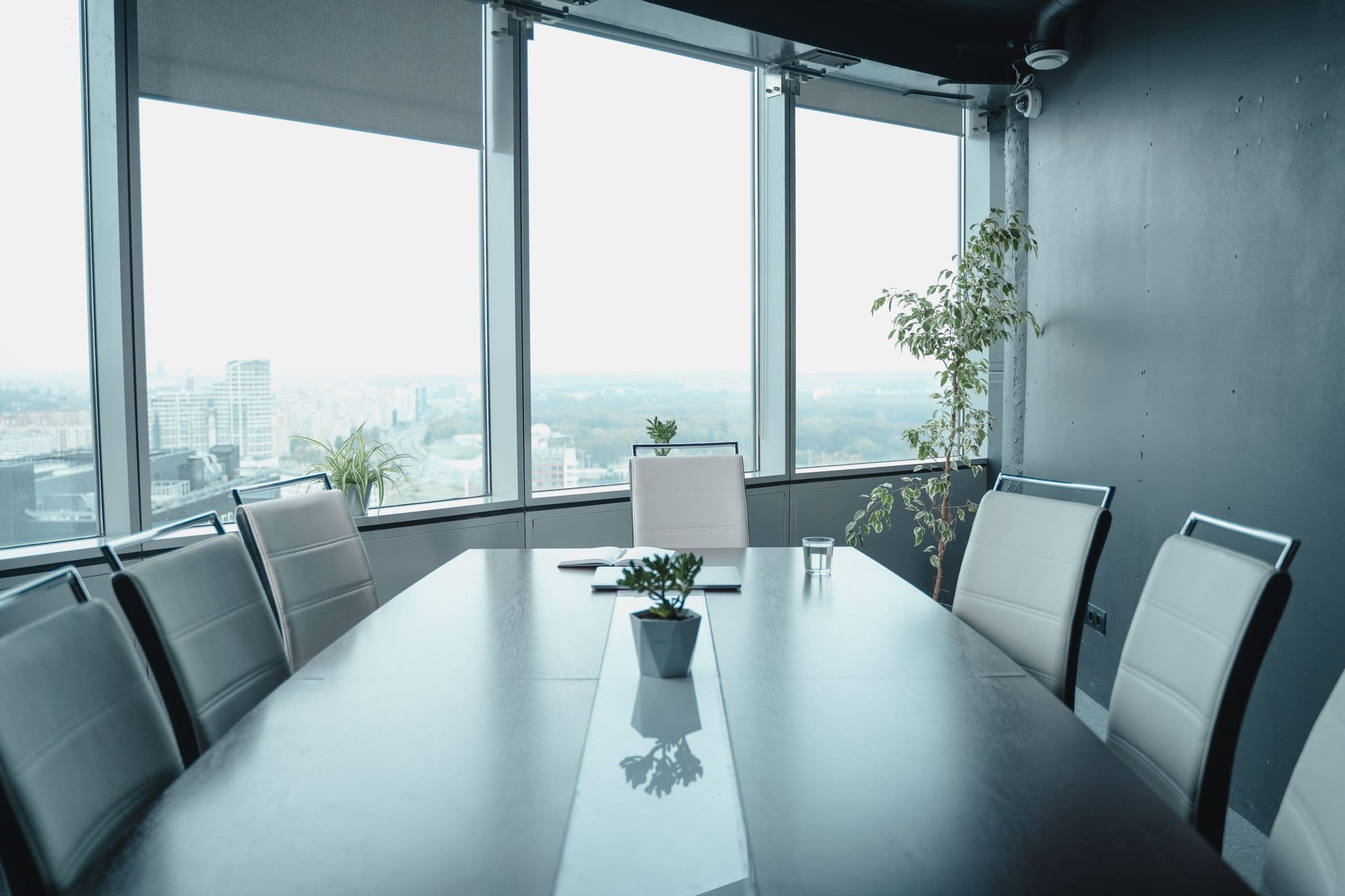 An empty meeting room with a long table and chairs facing tall windows over a city
